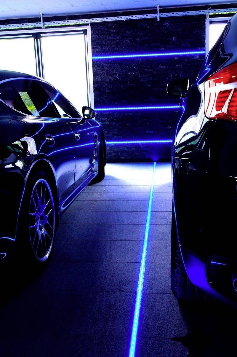 Due auto in un garage con una striscia LED blu sul pavimento tra di esse, che delimita chiaramente il posto auto. Sullo sfondo: parete nera con luci blu.