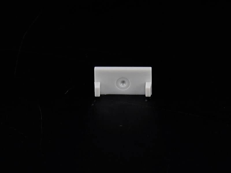 Un piccolo pezzo di plastica bianco con fori di fissaggio è posizionato su uno sfondo nero.