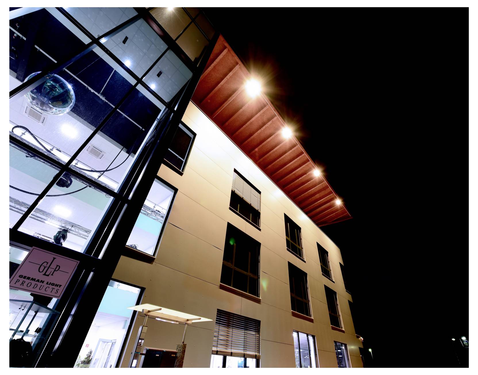 Esterno notturno di un moderno edificio per uffici con finestre illuminate e un ingresso in vetro, visto da una prospettiva ribassata contro un cielo scuro.