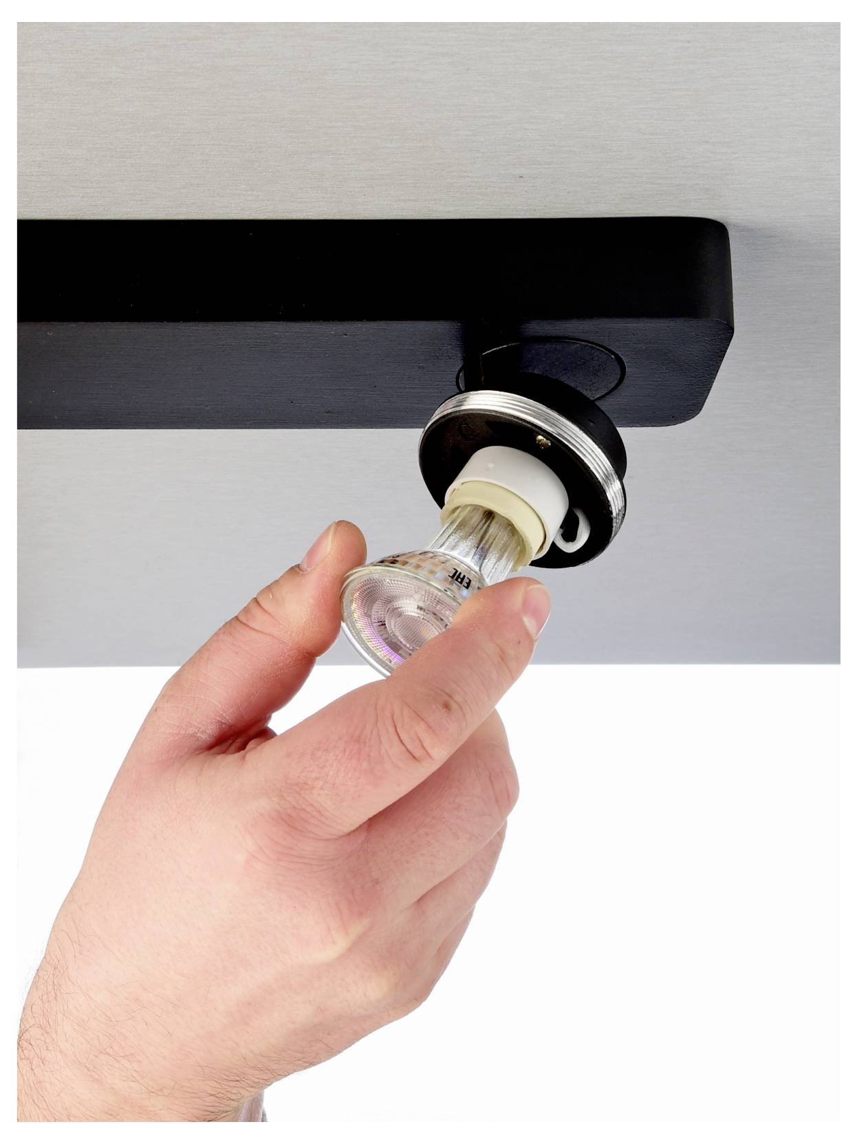 Mano che rimuove una lampadina da un plafoniera nera a soffitto.