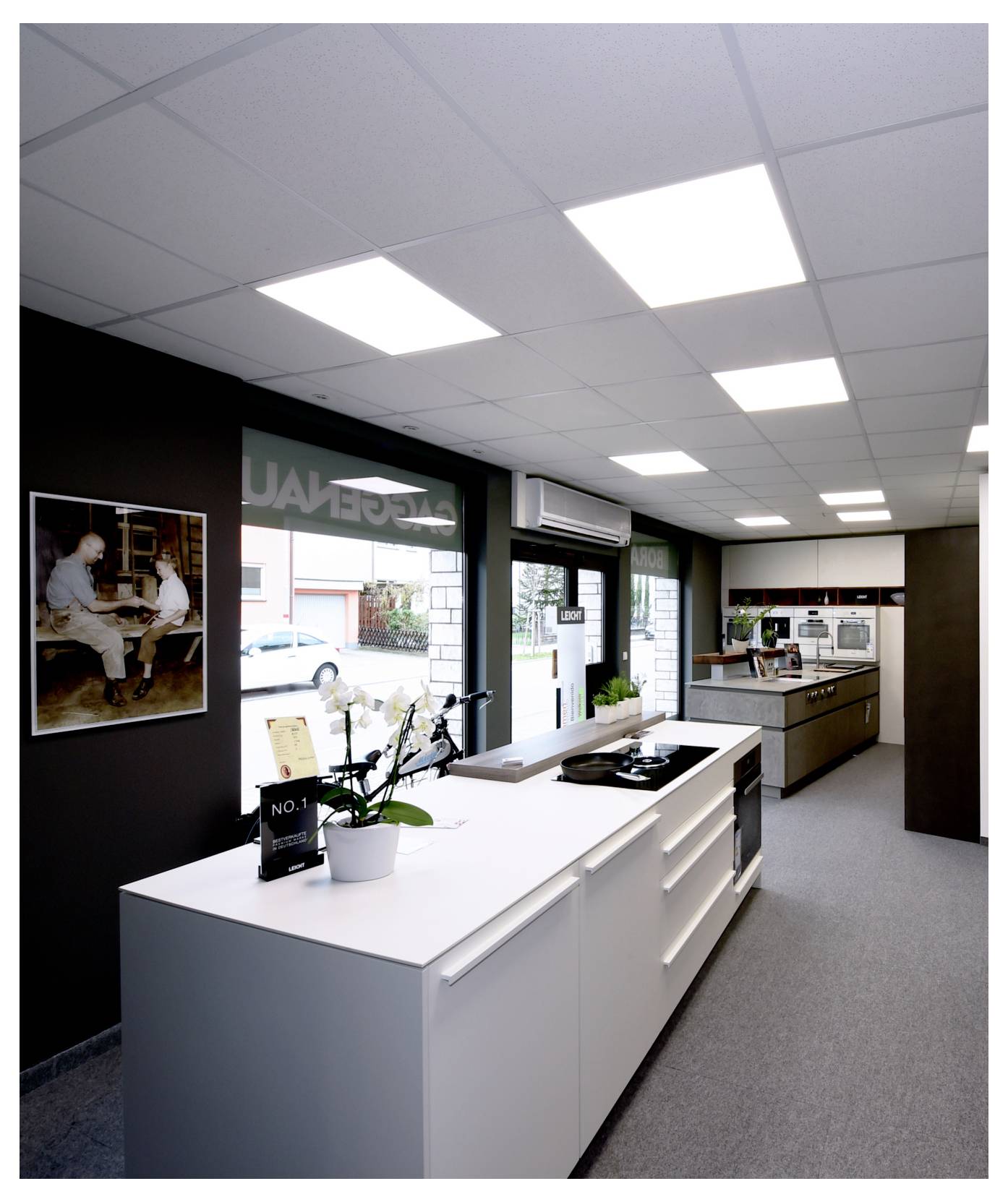 Cucina moderna da esposizione con isola bianca, luci a soffitto, vetrine espositive e un piano di lavoro sul fondo in uno spazio interno luminoso.