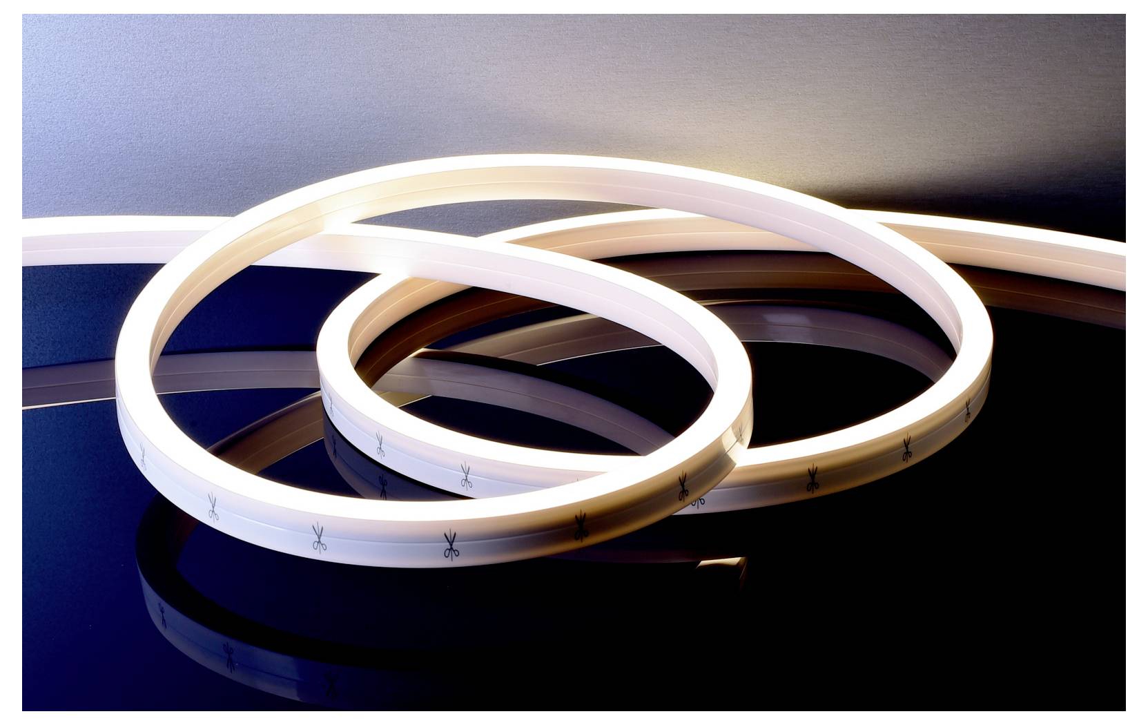 Striscia LED flessibile arrotolata che forma anelli luminosi sovrapposti su una superficie scura riflettente.