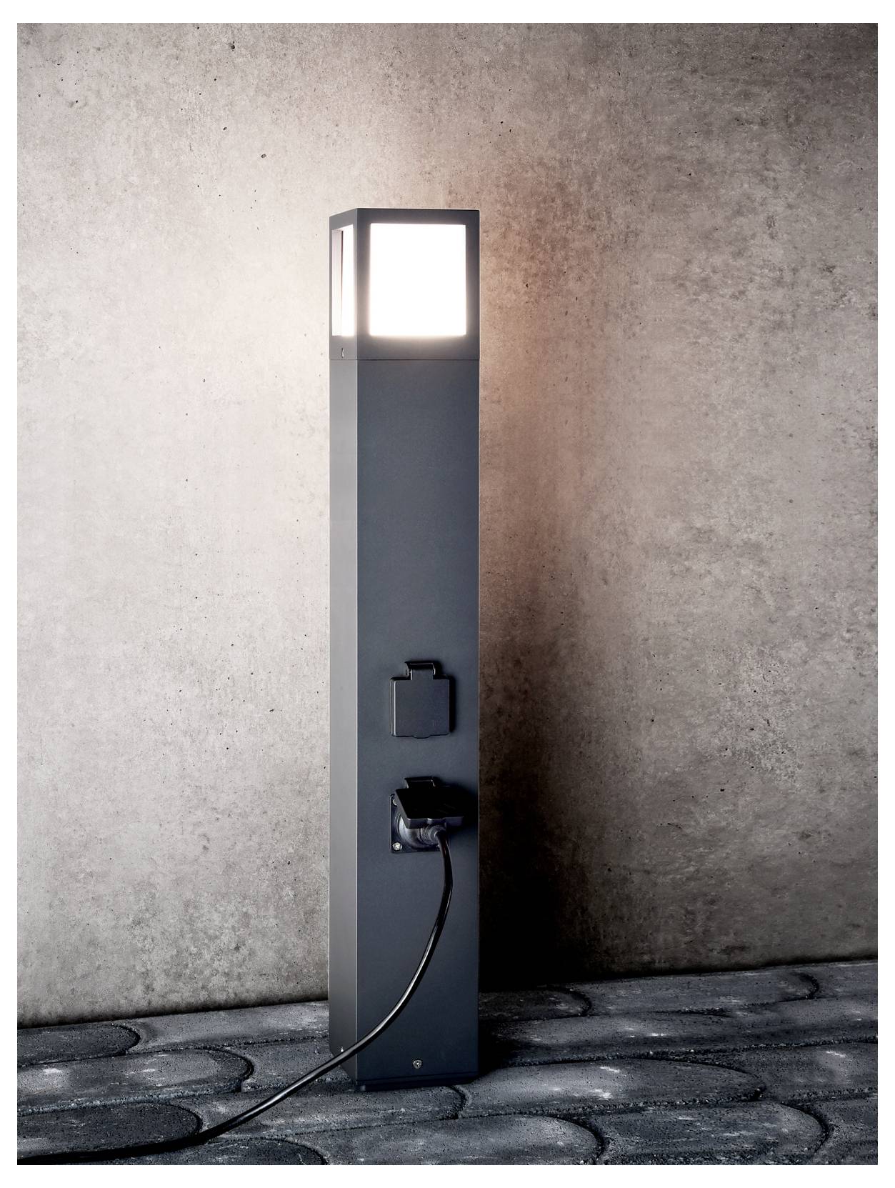 Colonnina di ricarica moderna per esterni con parte superiore illuminata e cavo di ricarica collegato, posizionata su un marciapiede in pietra davanti a una parete con texture.