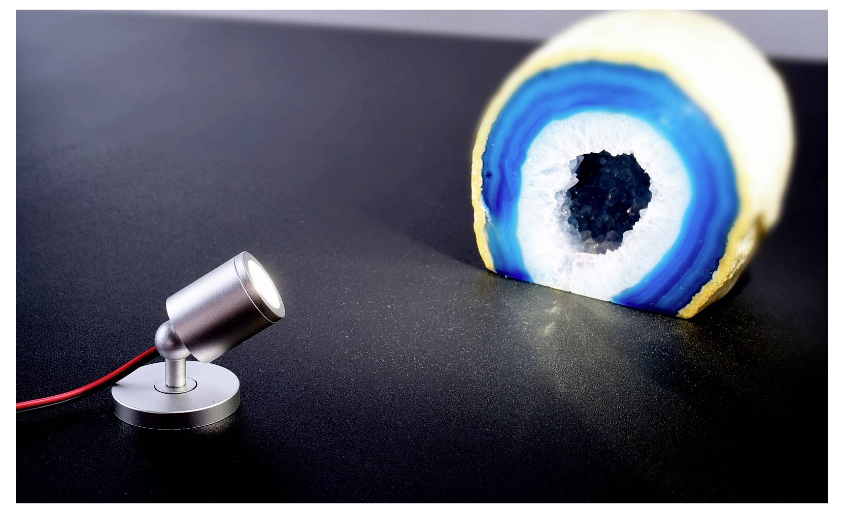Piccolo faretto che illumina una grande fetta di geode bianco e blu su una superficie scura.