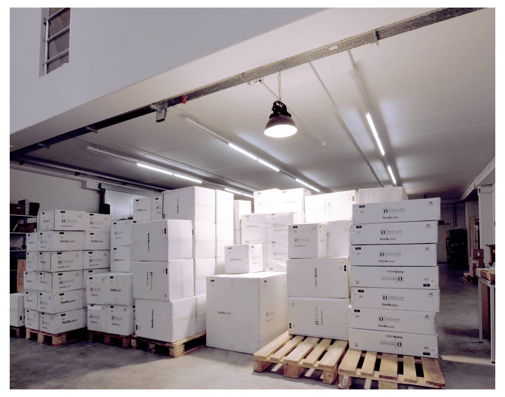 Area di stoccaggio di un magazzino con cataste di scatole di cartone bianche su pallet di legno sotto luci fluorescenti