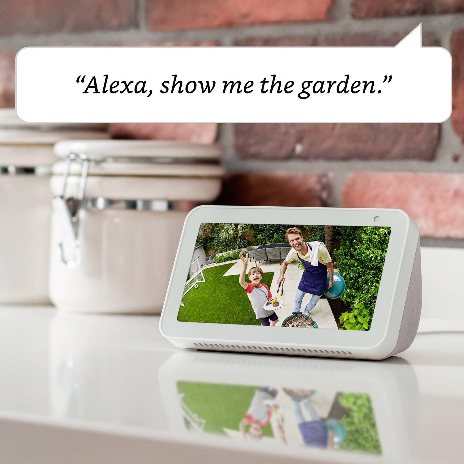 Un assistente vocale mostra una foto del giardino su uno schermo. Accanto c'è un fumetto con scritto 'Alexa, mostrami il giardino.'