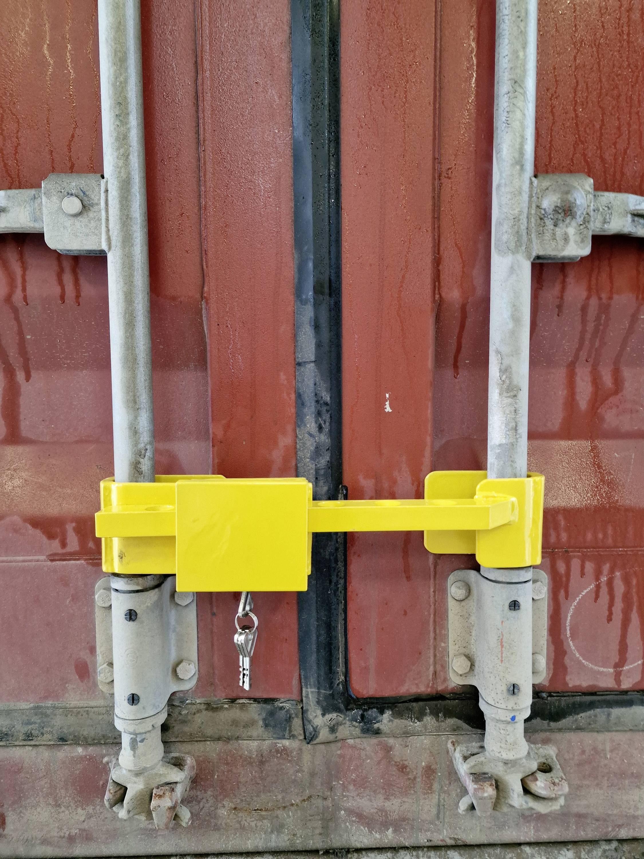 Un lucchetto di sicurezza giallo assicura le porte chiuse di un container rosso. Una chiave è appesa al lucchetto.