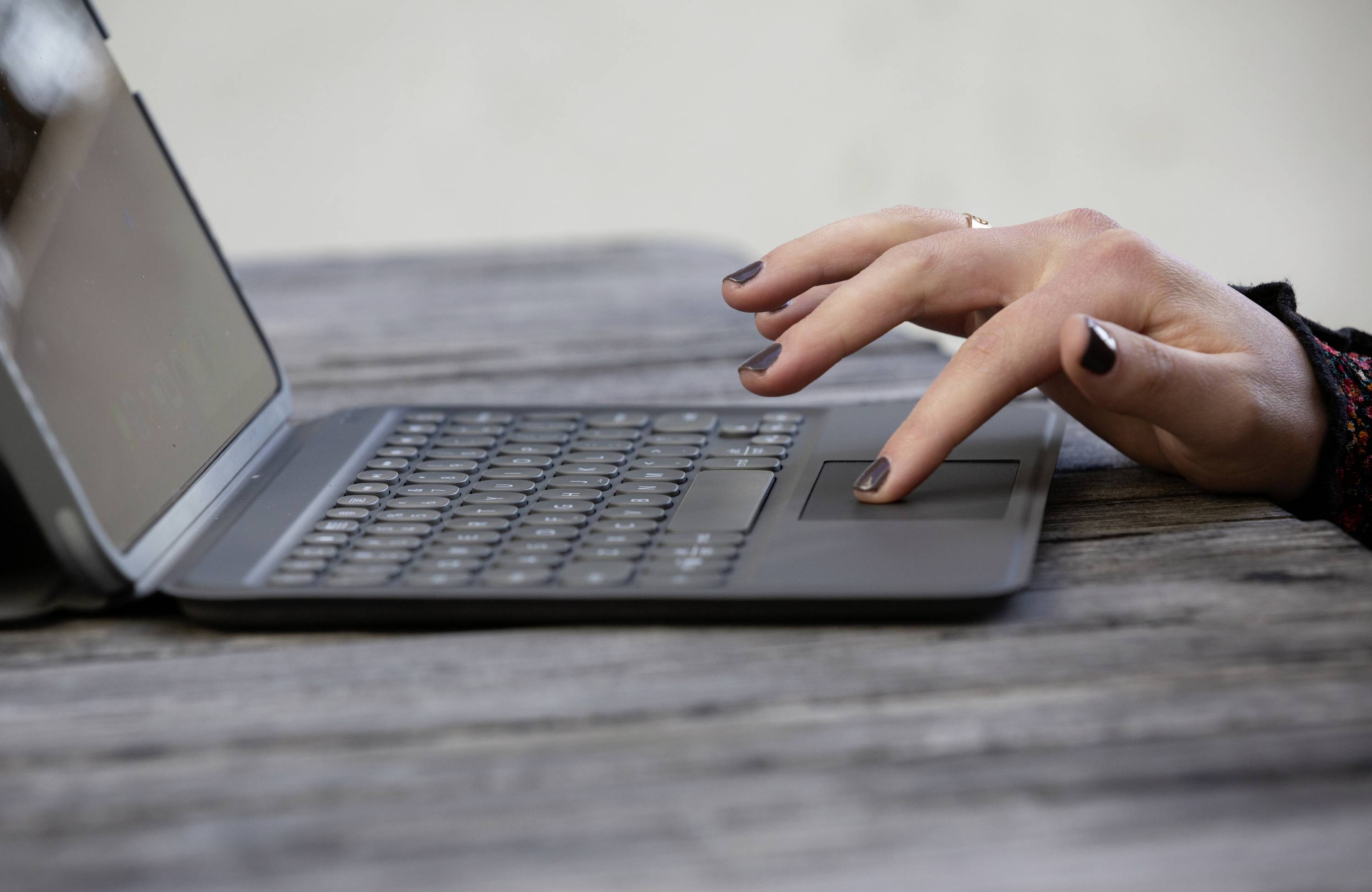 Una persona sta digitando su un laptop poggiato su un tavolo di legno all'aperto. Mani a fuoco, custodia in plastica grigia, ambiente tranquillo.
