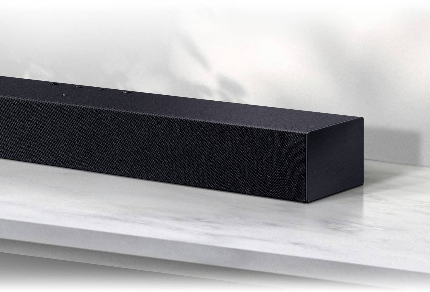 Soundbar nera su un tavolo di marmo bianco davanti a una parete bianca. Forma rettangolare, design moderno e minimale.