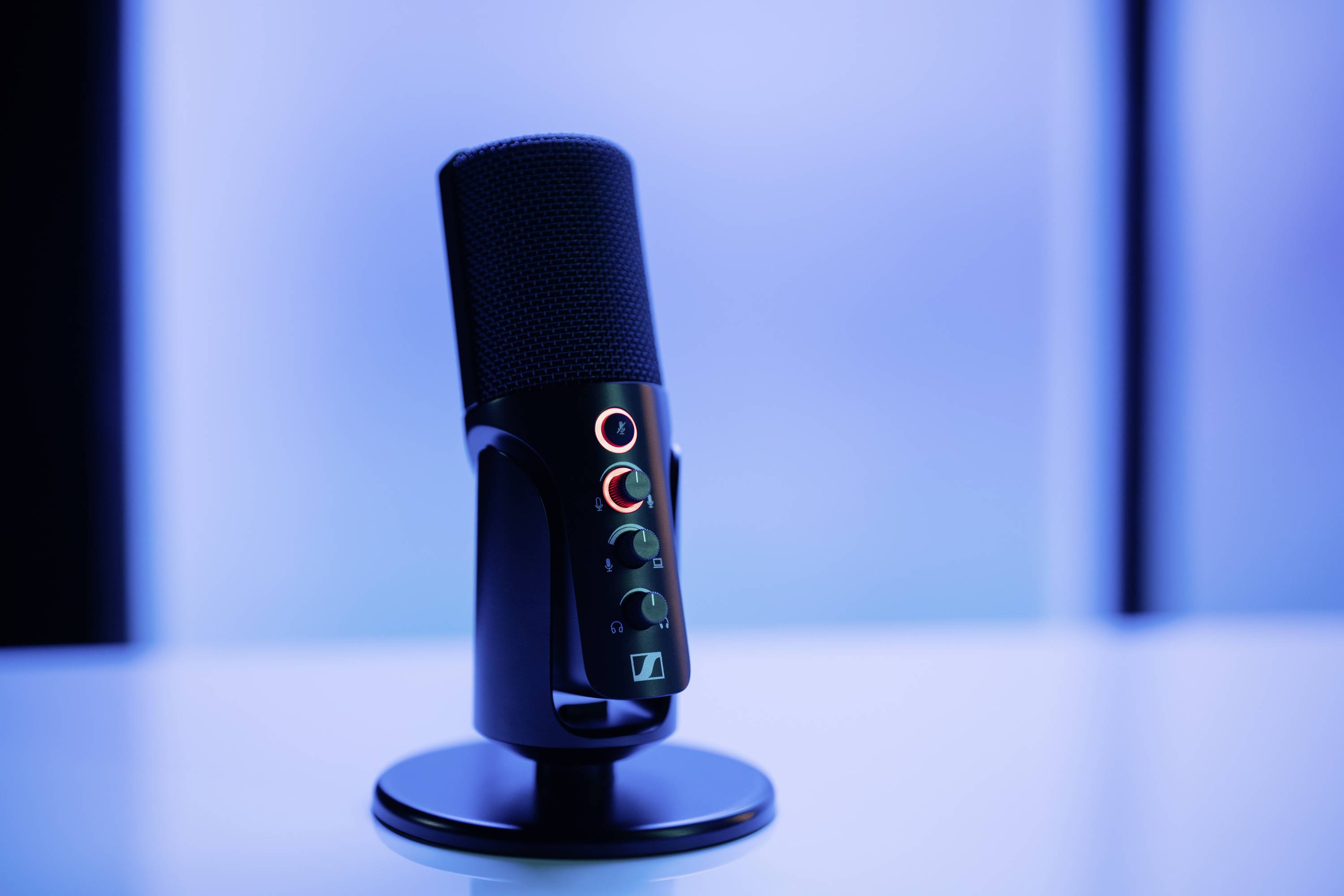 Un microfono nero con un supporto è posizionato su un tavolo davanti a uno sfondo blu sfocato.