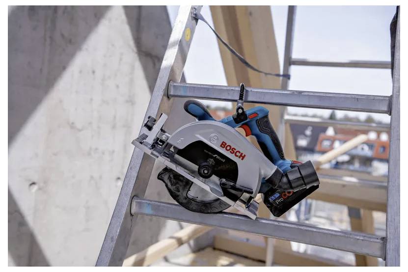 Un seghetto circolare Bosch è montato su una scala metallica in un cantiere edile. Travi di legno e un edificio sono visibili sullo sfondo.