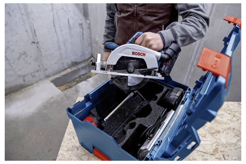 Una persona che inserisce una sega circolare Bosch in un contenitore blu con inserti in schiuma personalizzati su una superficie in legno, sullo sfondo di un muro in calcestruzzo.