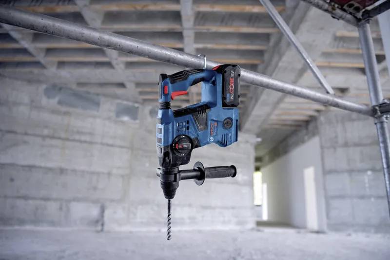 Un trapano elettrico blu è appeso a un'impalcatura metallica in un'ampia stanza in cemento non finita, evidenziando la sua utilità nel lavoro edile.