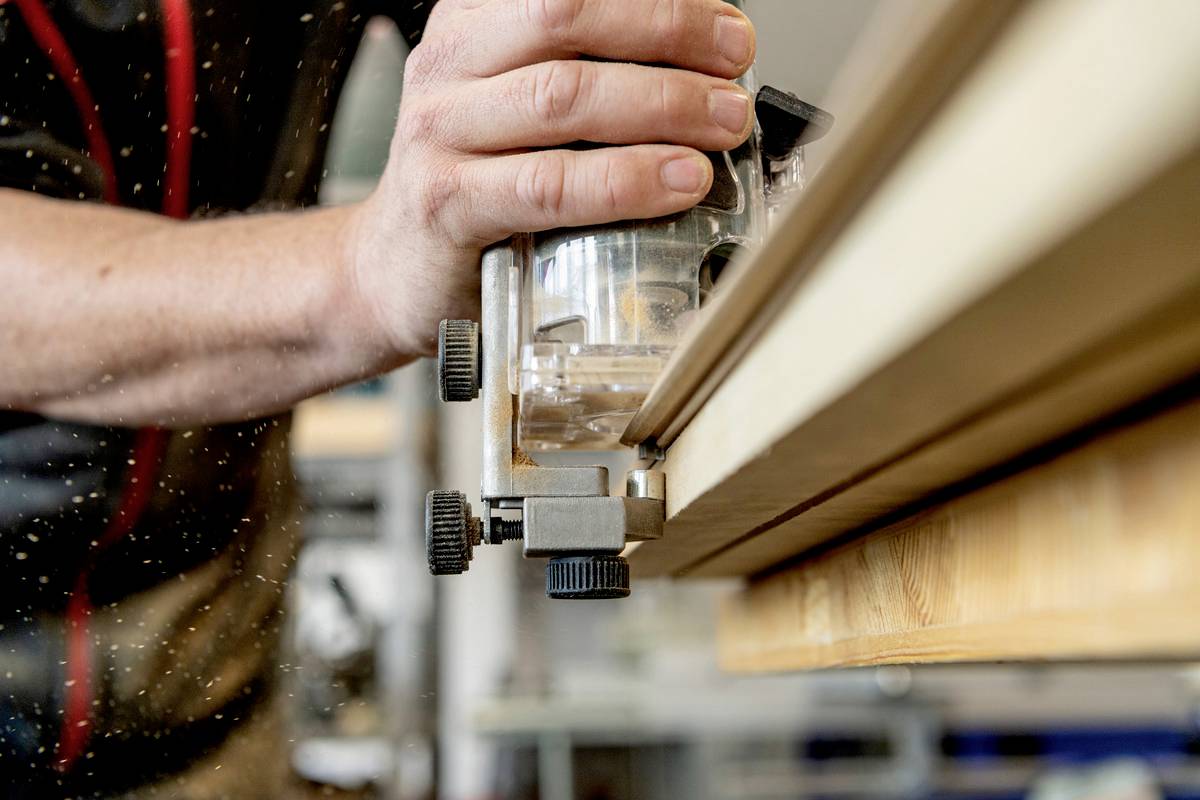 Una persona sta lavorando con una macchina per la lavorazione del legno e leviga il bordo di un'asse di legno. Trucioli di segatura volano nell'aria.
