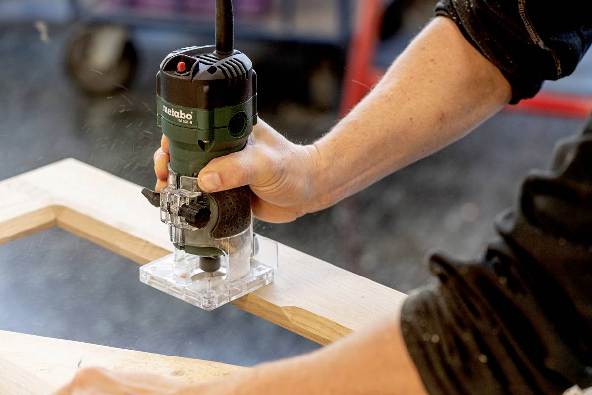 Una persona sta utilizzando una fresatrice per lavorare una tavola di legno. Trucioli di legno volano nell'officina.