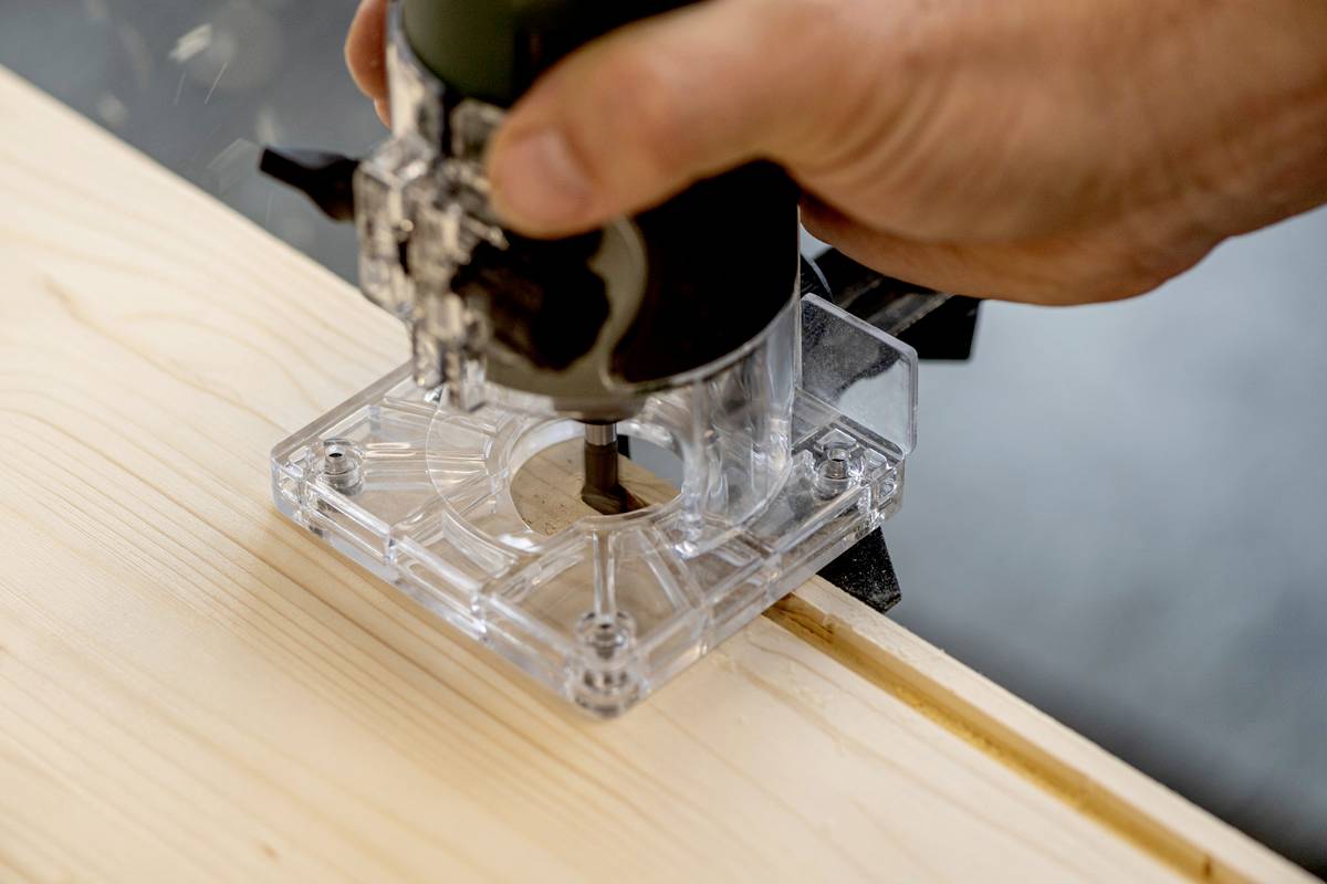 Una persona sta utilizzando una fresatrice su un pannello di legno. La fresa è trasparente e contribuisce alla lavorazione del legno.