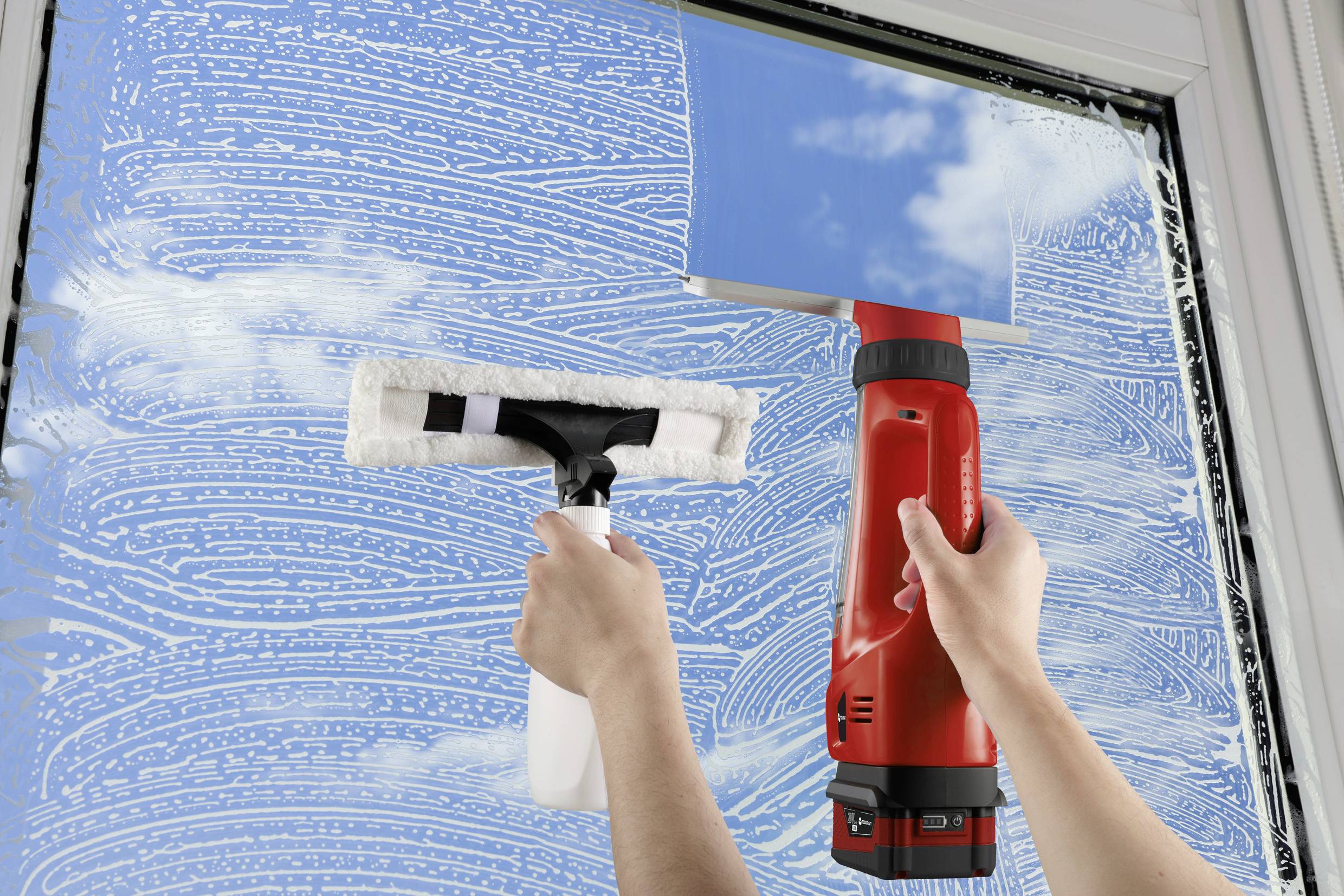 Una persona sta pulendo un vetro con uno spray detergente e un tergivetro. Il cielo si riflette nel vetro, le nuvole sono visibili.