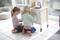 Due bambini giocano con una cucina giocattolo. Sono seduti su un pavimento di piastrelle bianche e si occupano delle ante degli armadi.