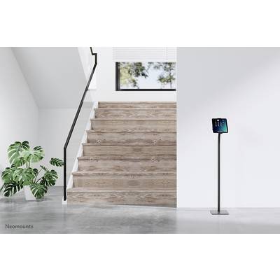 Scala con gradini in legno in uno spazio minimalista, accanto un tablet su un supporto. Una grande pianta sulla sinistra.