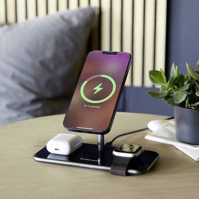Uno smartphone, delle cuffie e uno smartwatch vengono caricati senza fili su un caricabatterie. Sullo sfondo c'è una pianta.