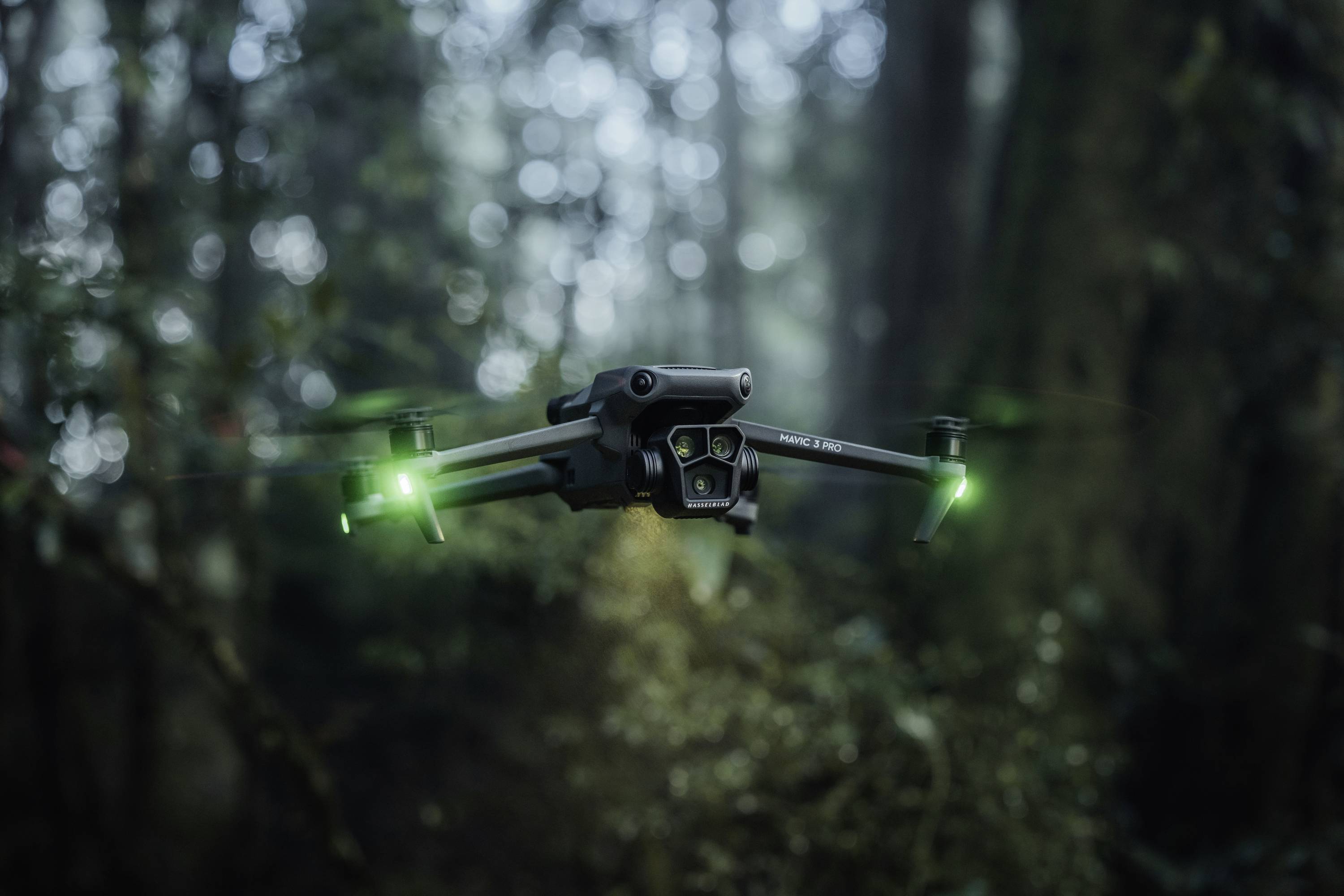 Drone con luci verdi brillanti aleggia in una foresta nebbiosa, circondato da alberi sfocati.