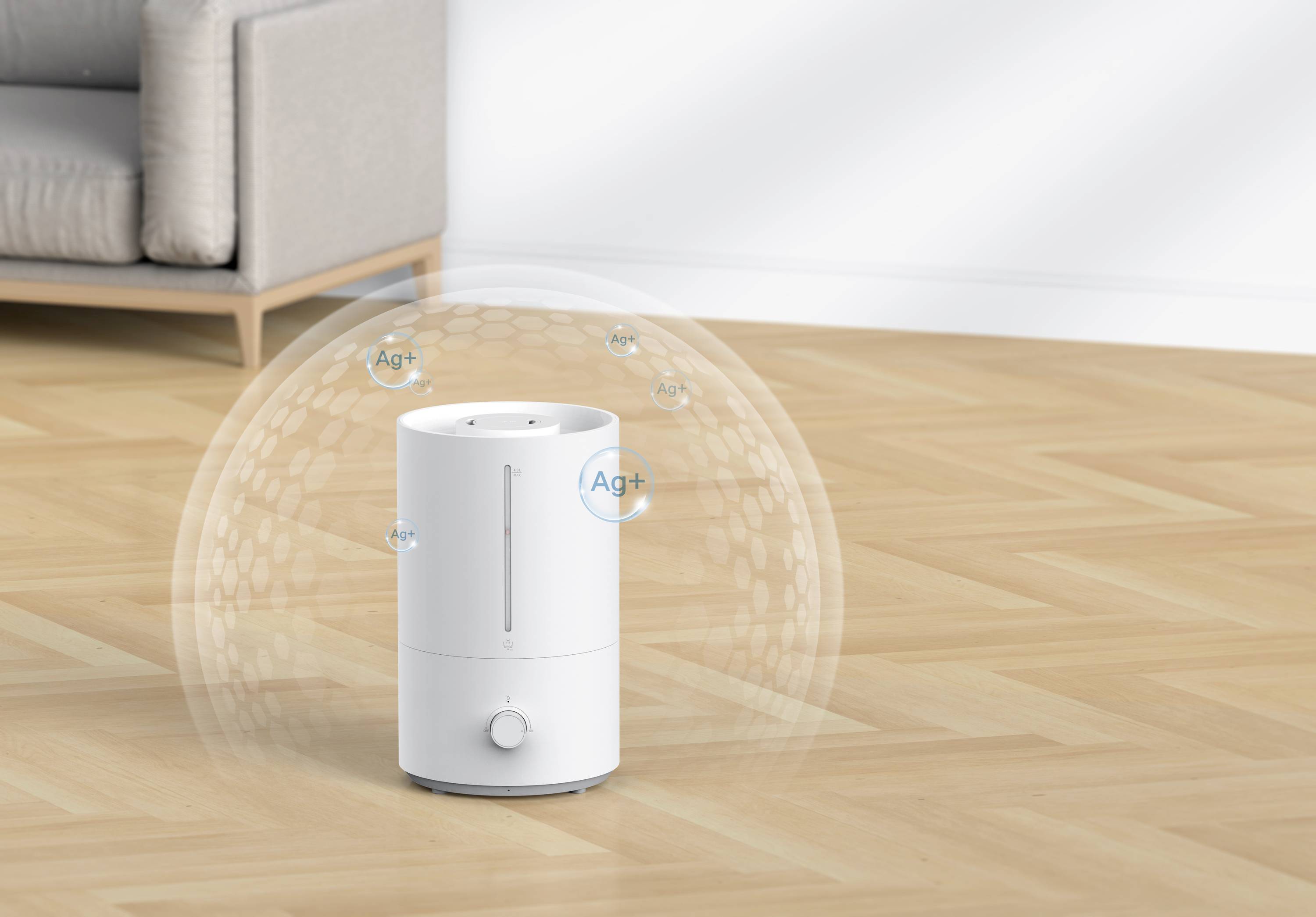 Un umidificatore bianco è posizionato su un pavimento in legno in una stanza con un divano. Bolle con 'Ag+' galleggiano intorno all'umidificatore.