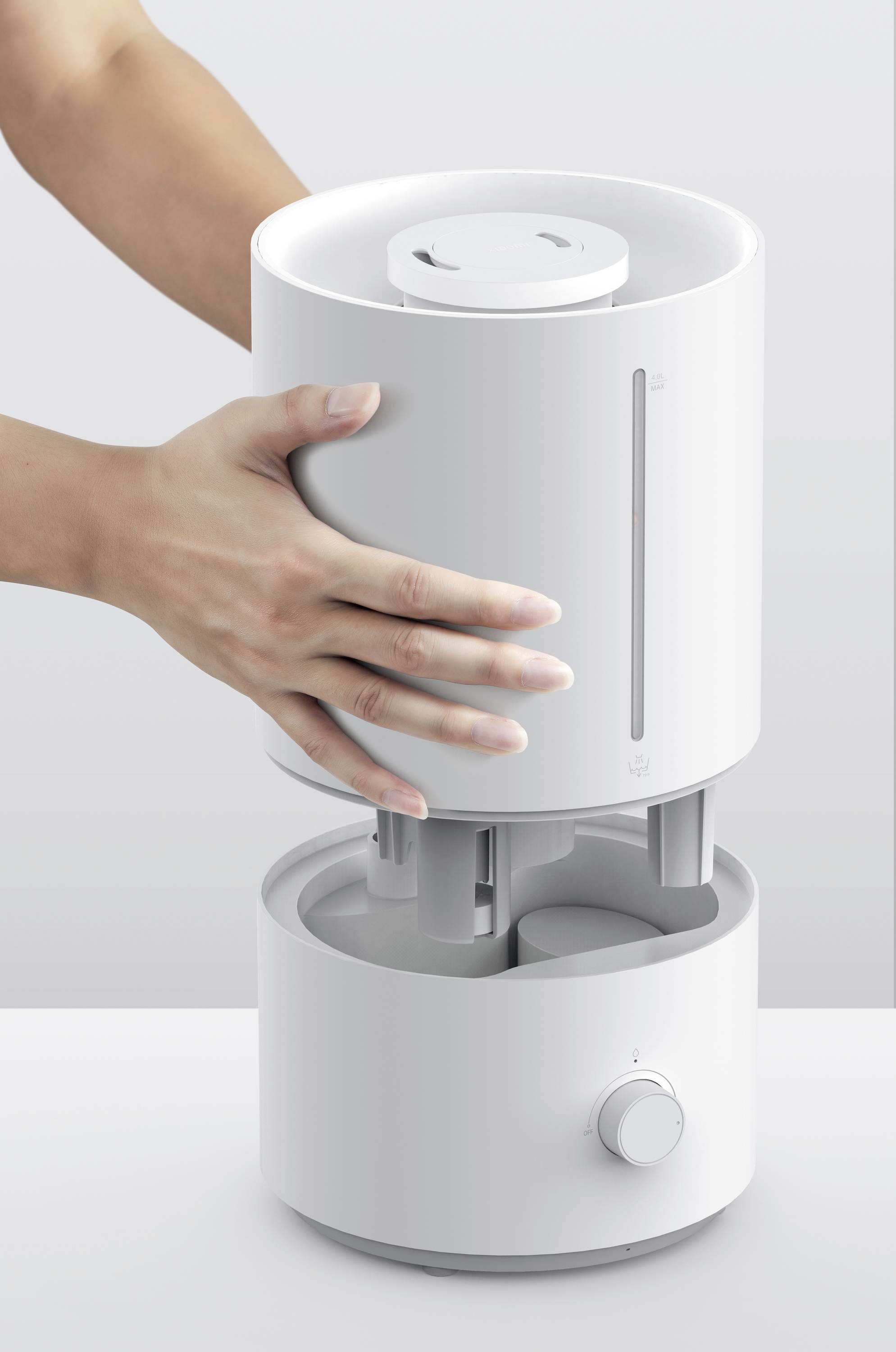 Una persona apre un umidificatore bianco rimuovendo la parte superiore. L'umidificatore ha un design semplice e moderno.