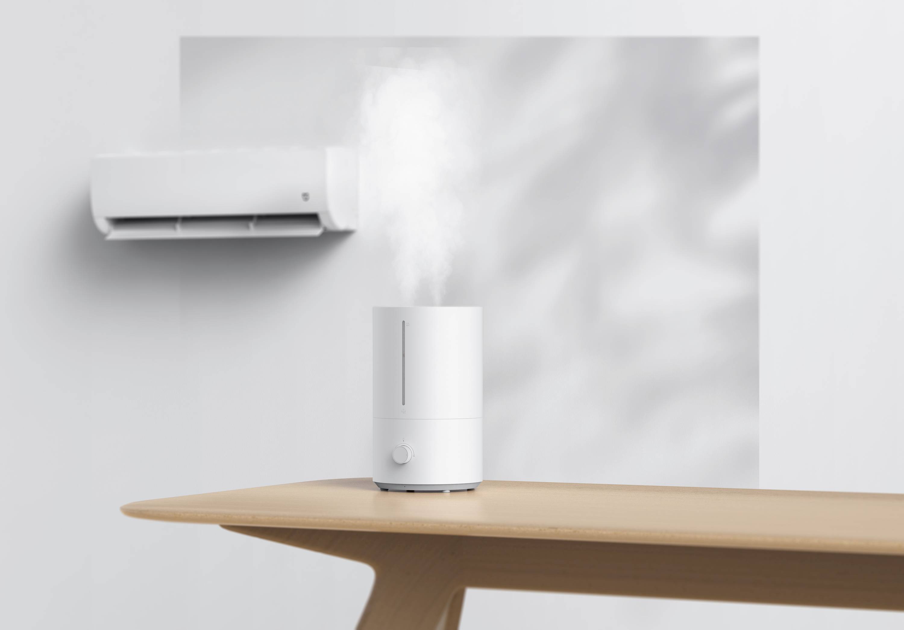 Un umidificatore su un tavolo di legno emette vapore. Sullo sfondo si vede un condizionatore su una parete bianca.