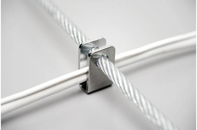 Morsetto metallico tiene insieme due funi metalliche ad angolo retto. Metallo forte e lucente su sfondo grigio.