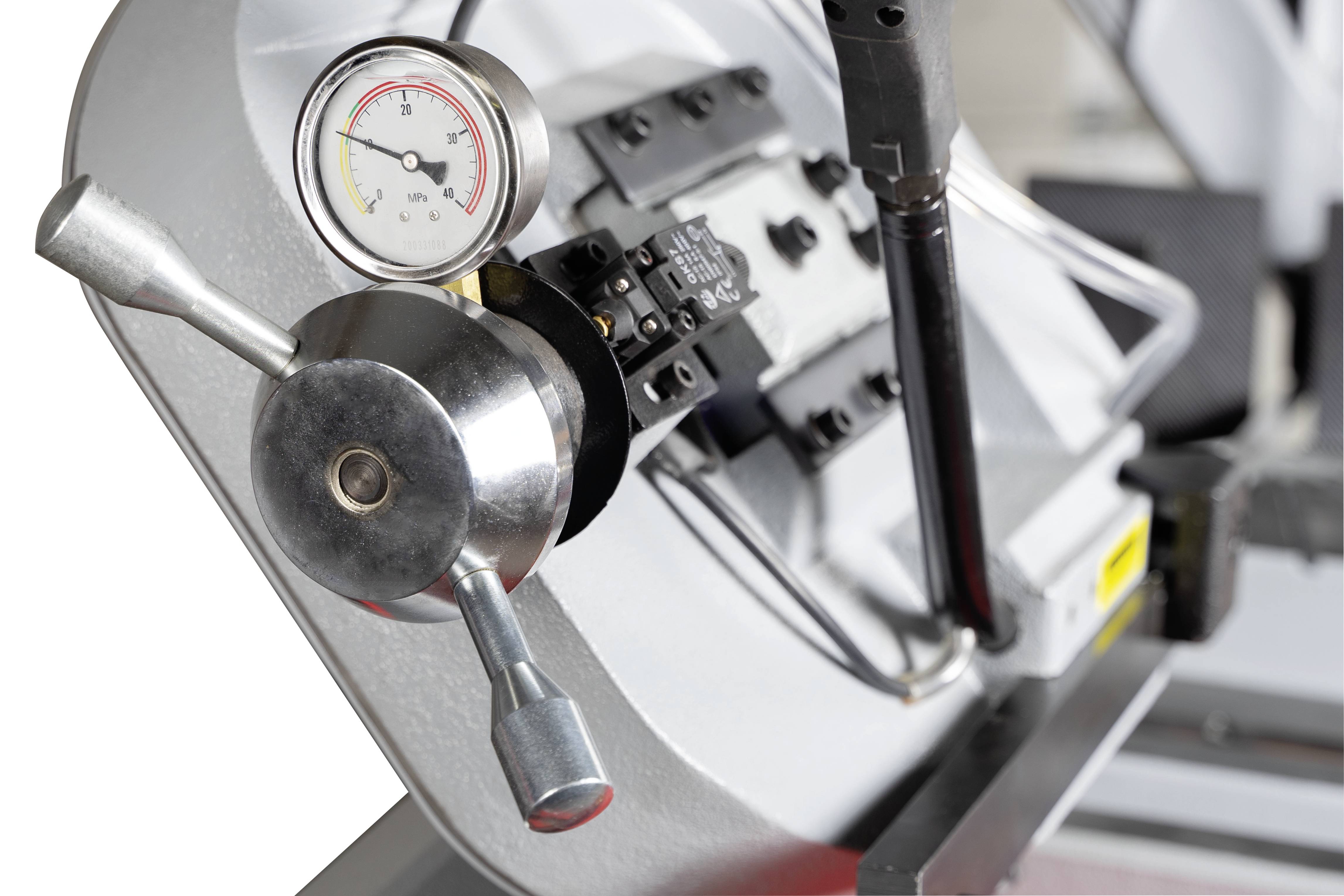 Primo piano di una macchina metallica con manometro e leva. La macchina è probabilmente utilizzata per lavori di precisione nell'industria.