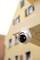 Telecamera di sicurezza su una trave di legno beige, con un edificio giallo sullo sfondo.