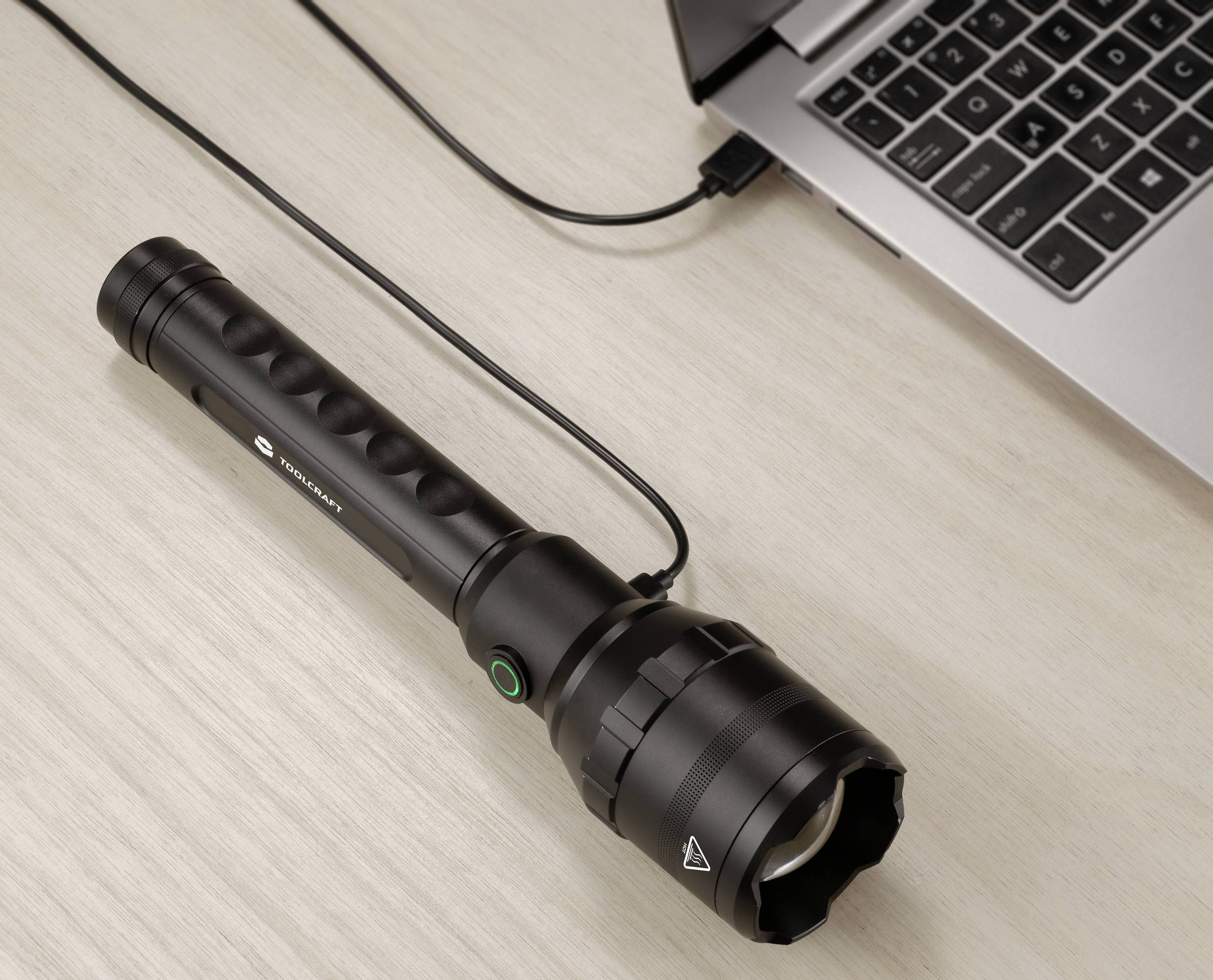 Una torcia nera è collegata a un laptop tramite un cavo USB, posizionata su un tavolo di legno.