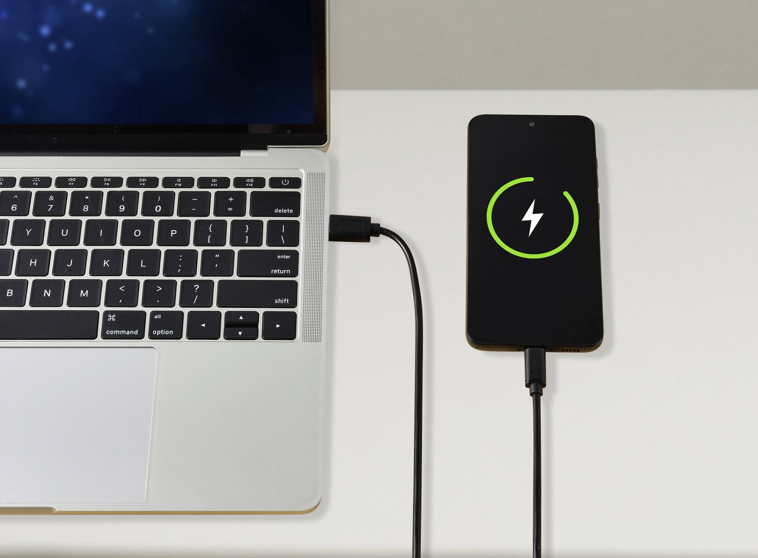 Un laptop è collegato a uno smartphone che sta caricando. Il display dello smartphone mostra un'icona di ricarica.