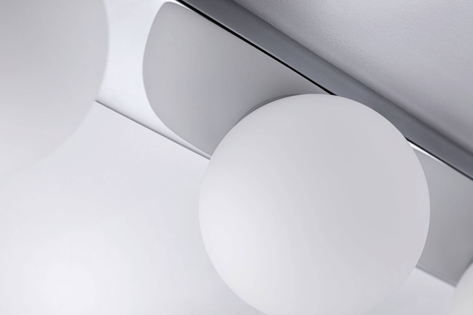 Lampada bianca e sferica montata sul soffitto, ripresa da vicino. Design moderno e minimale con un supporto liscio e argentato.
