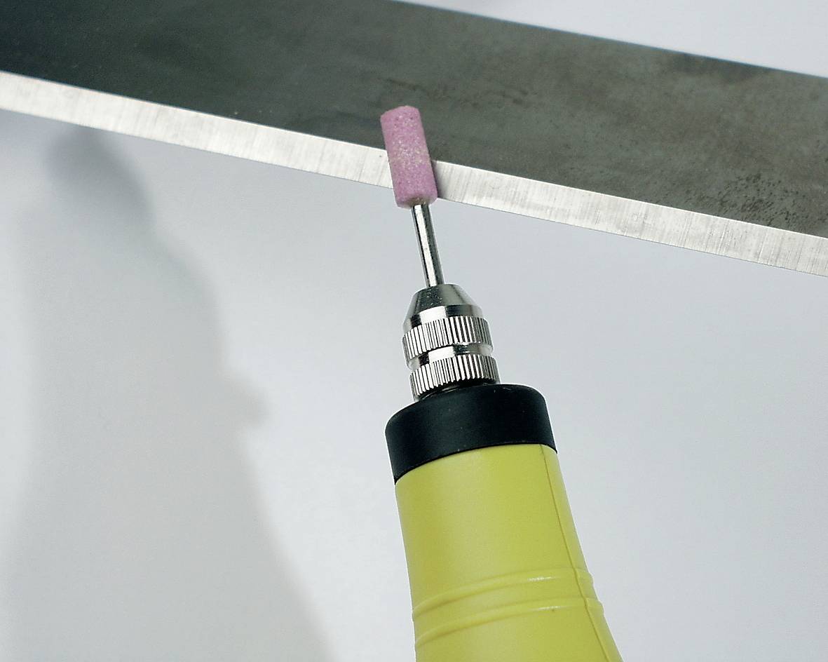 Un utensile giallo con una testina abrasiva rotante rosa sta lavorando il bordo di un pezzo di metallo.