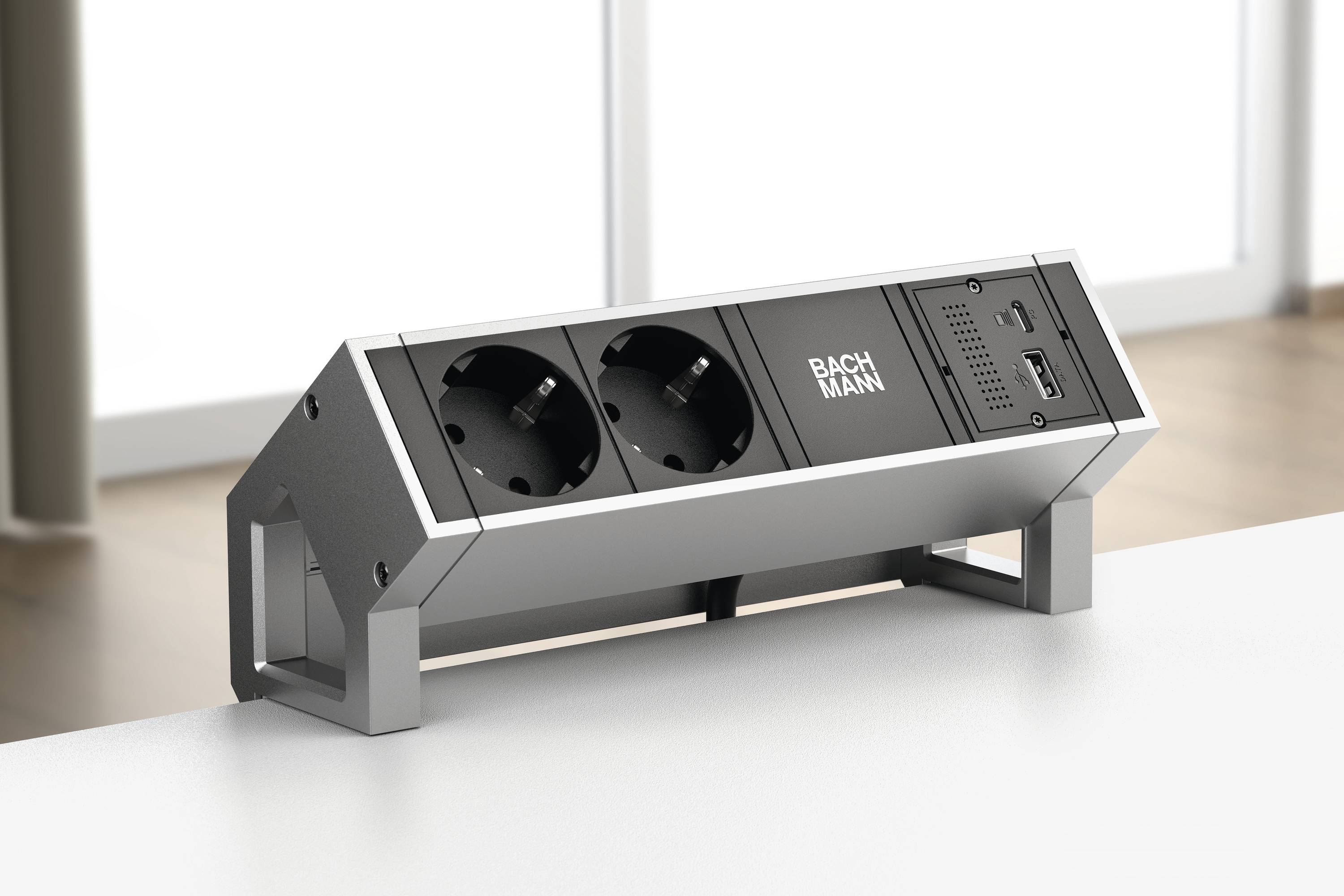 Multipresa con due prese Schuko e porta USB su un tavolo. Sullo sfondo finestre con luce diurna diffusa.