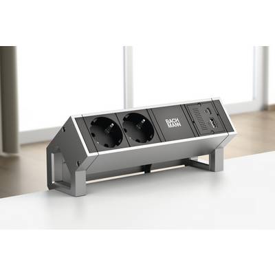 Multipresa con due prese Schuko e porta USB su un tavolo. Sullo sfondo finestre con luce diurna diffusa.