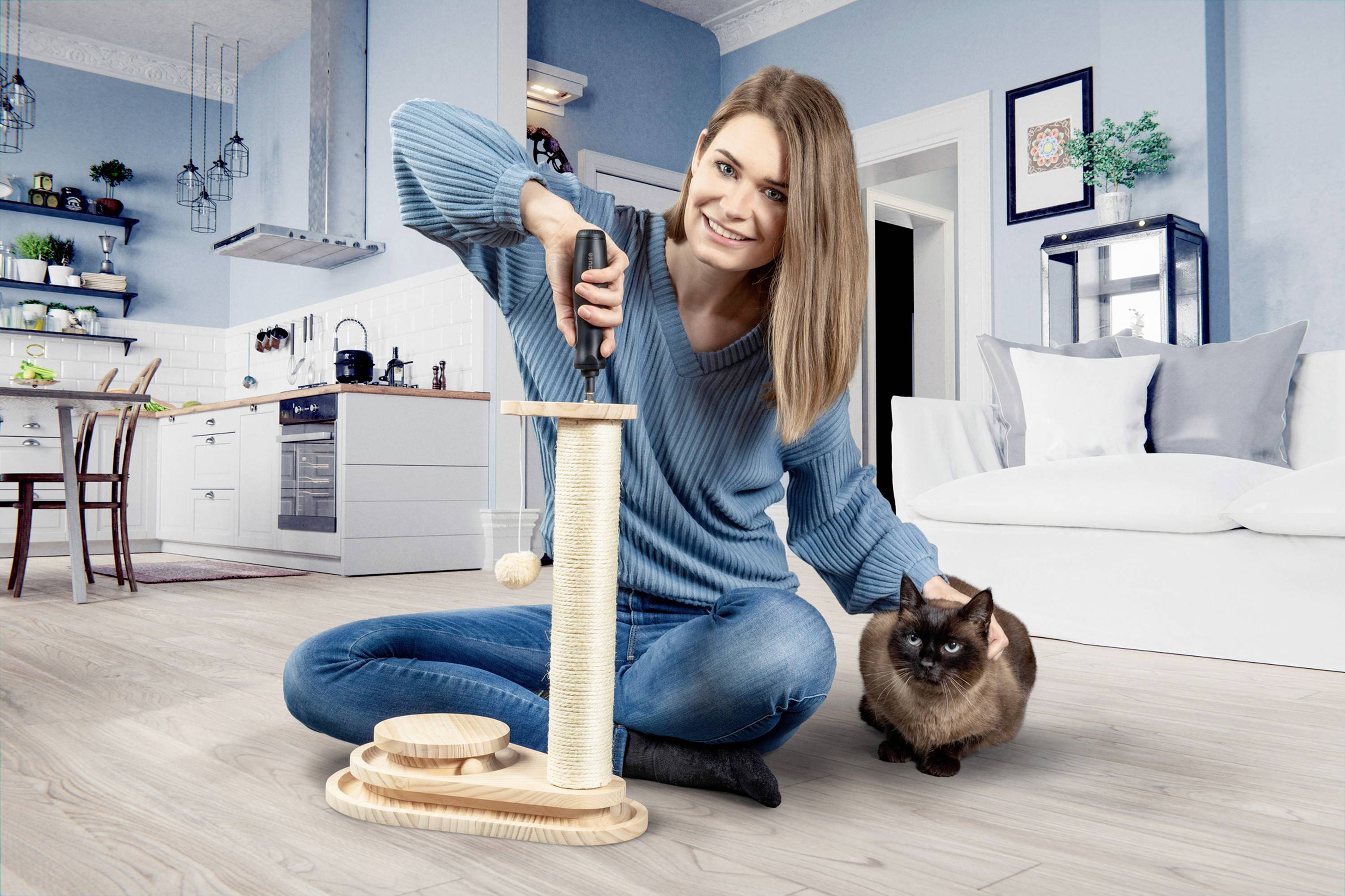 Una donna con un maglione blu è seduta sul pavimento e gioca con un gatto. Sta utilizzando un giocattolo per gatti in soggiorno.