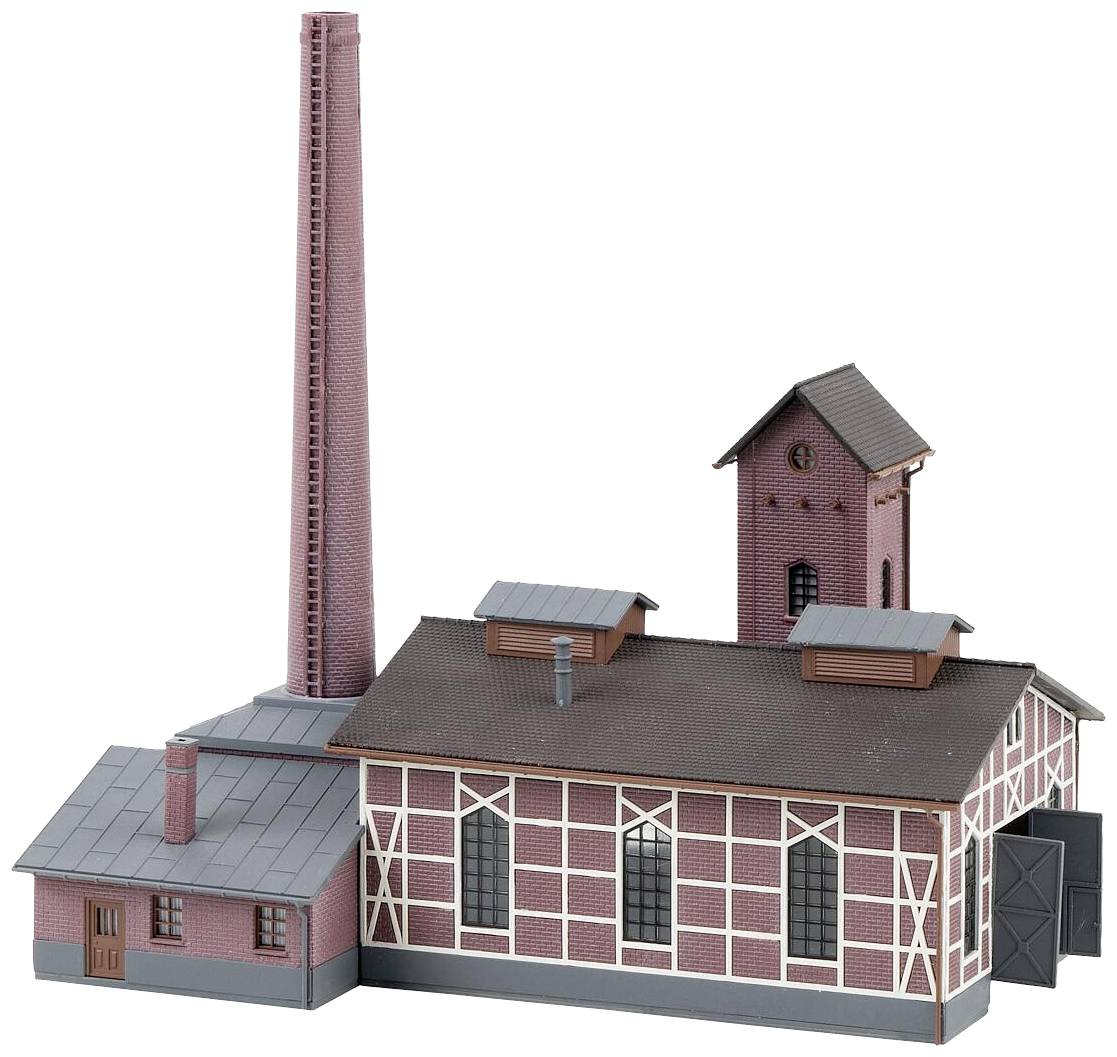 Un modello di una fabbrica storica con un alto camino, diversi edifici con facciate in mattoni e tetti a due falde.