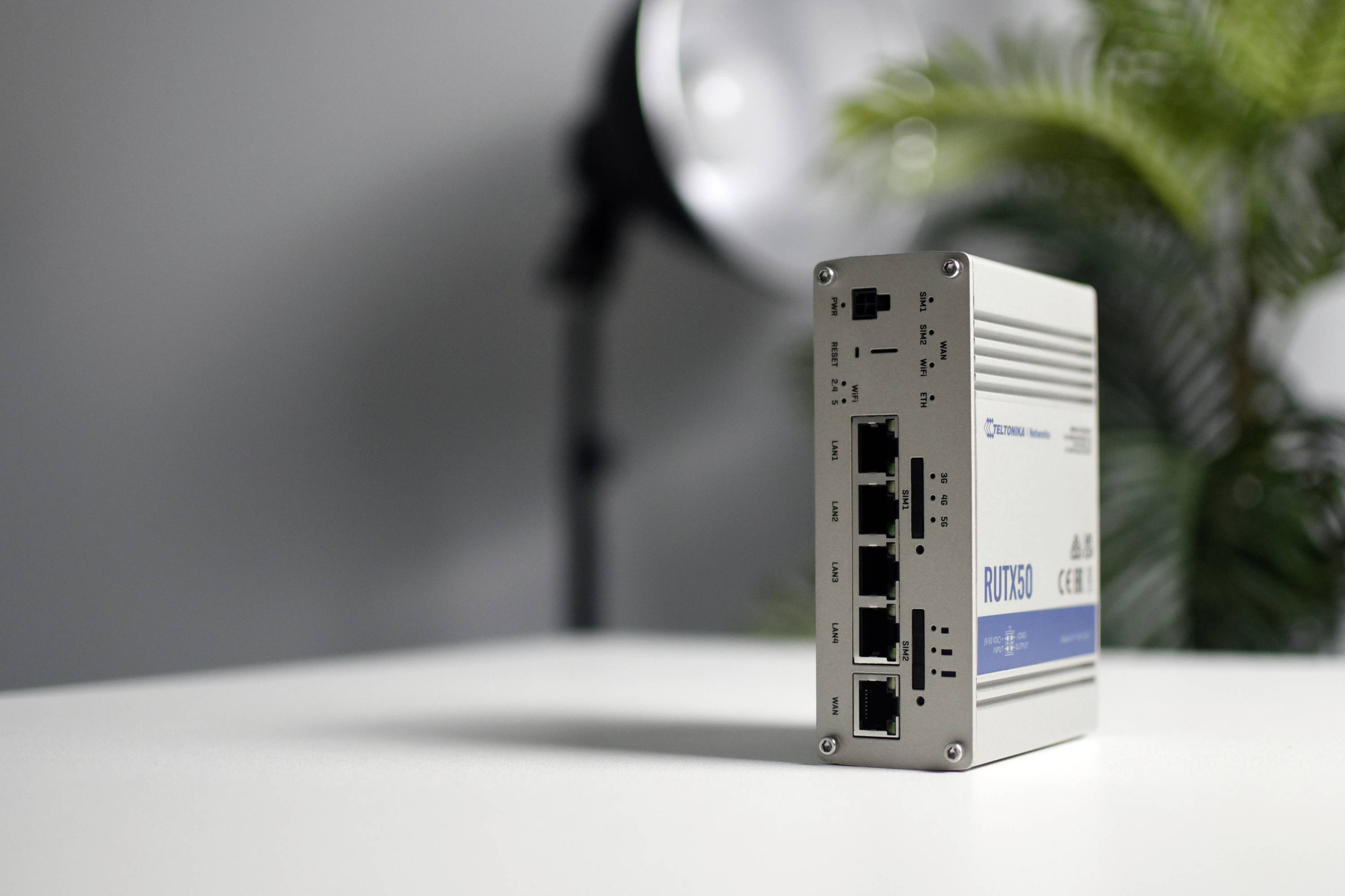 Router industriali con più porte Ethernet su un tavolo, con piante sfocate sullo sfondo e luce da studio.