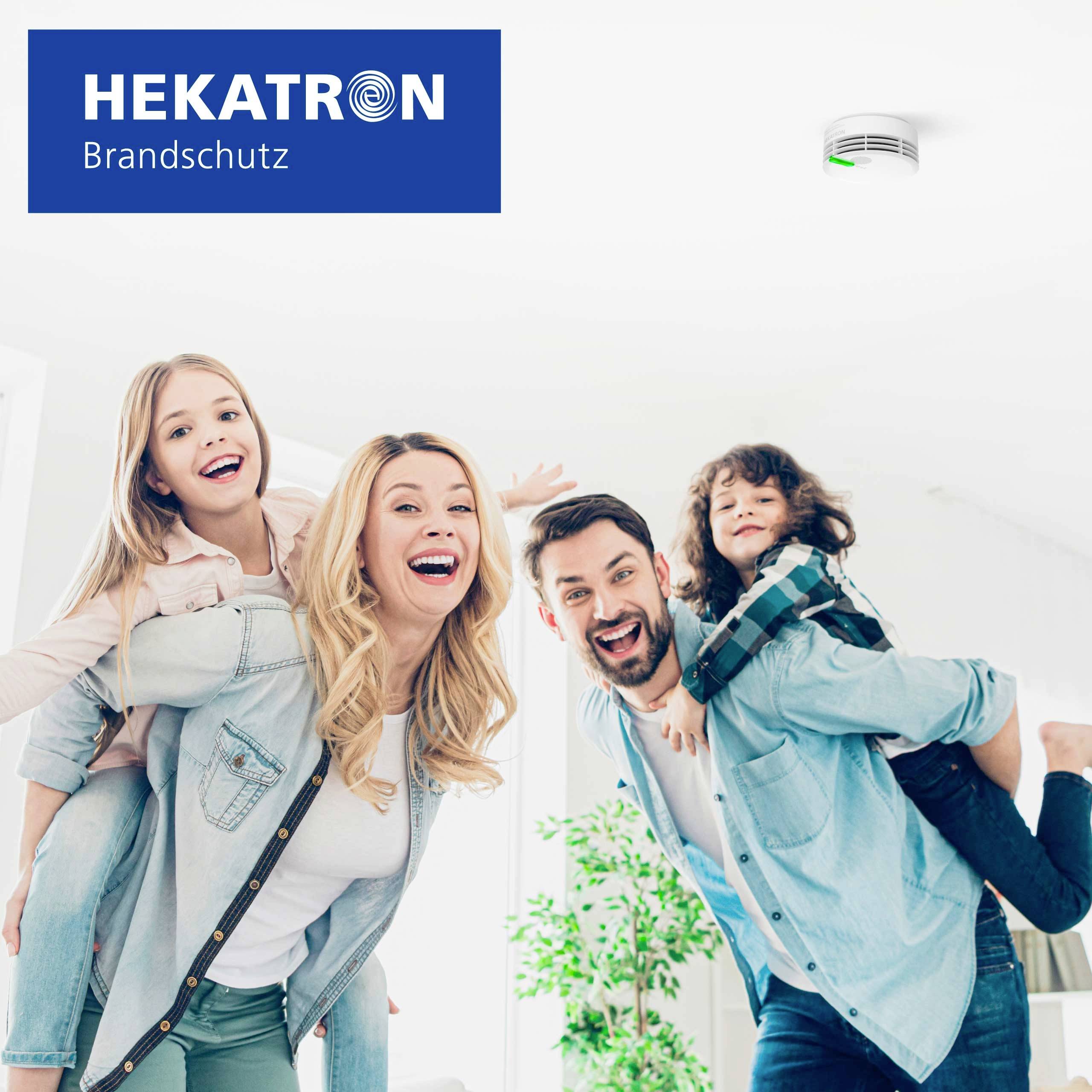 Una famiglia di quattro persone sorridenti sotto un rilevatore di fumo a soffitto, che evidenzia la sicurezza domestica. Il logo di 'Hekatron Brandschutz' è visibile.