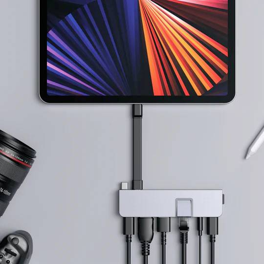 Un tablet con schermo luminoso è collegato tramite un hub USB-C a diversi dispositivi, tra cui una fotocamera e una penna.