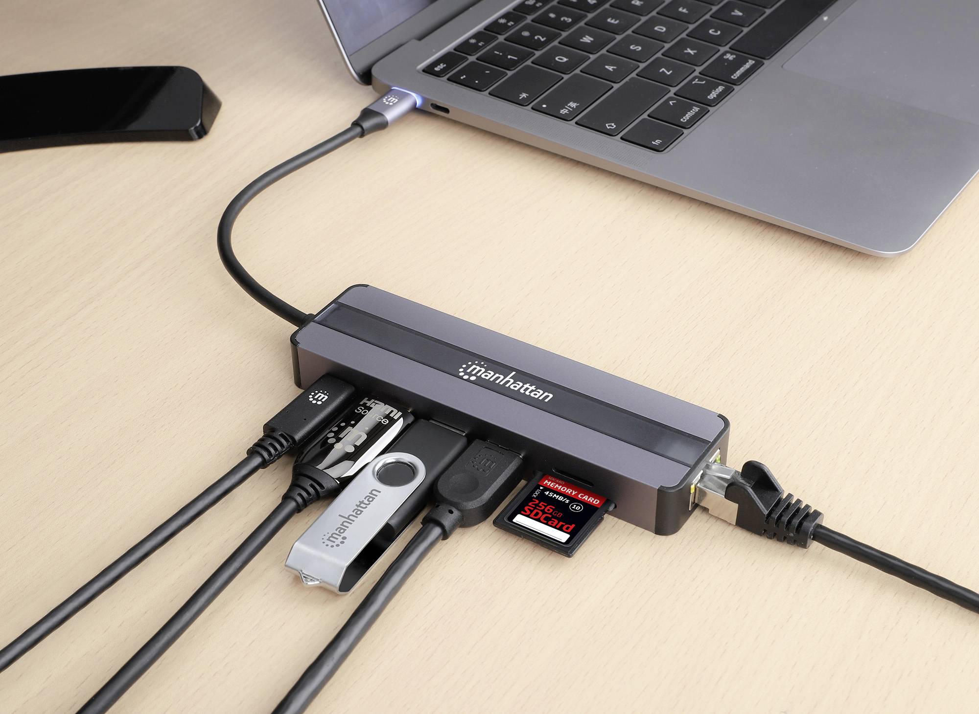 Un laptop è collegato a un hub che ospita diversi cavi e supporti di archiviazione come chiavette USB e una scheda SD.