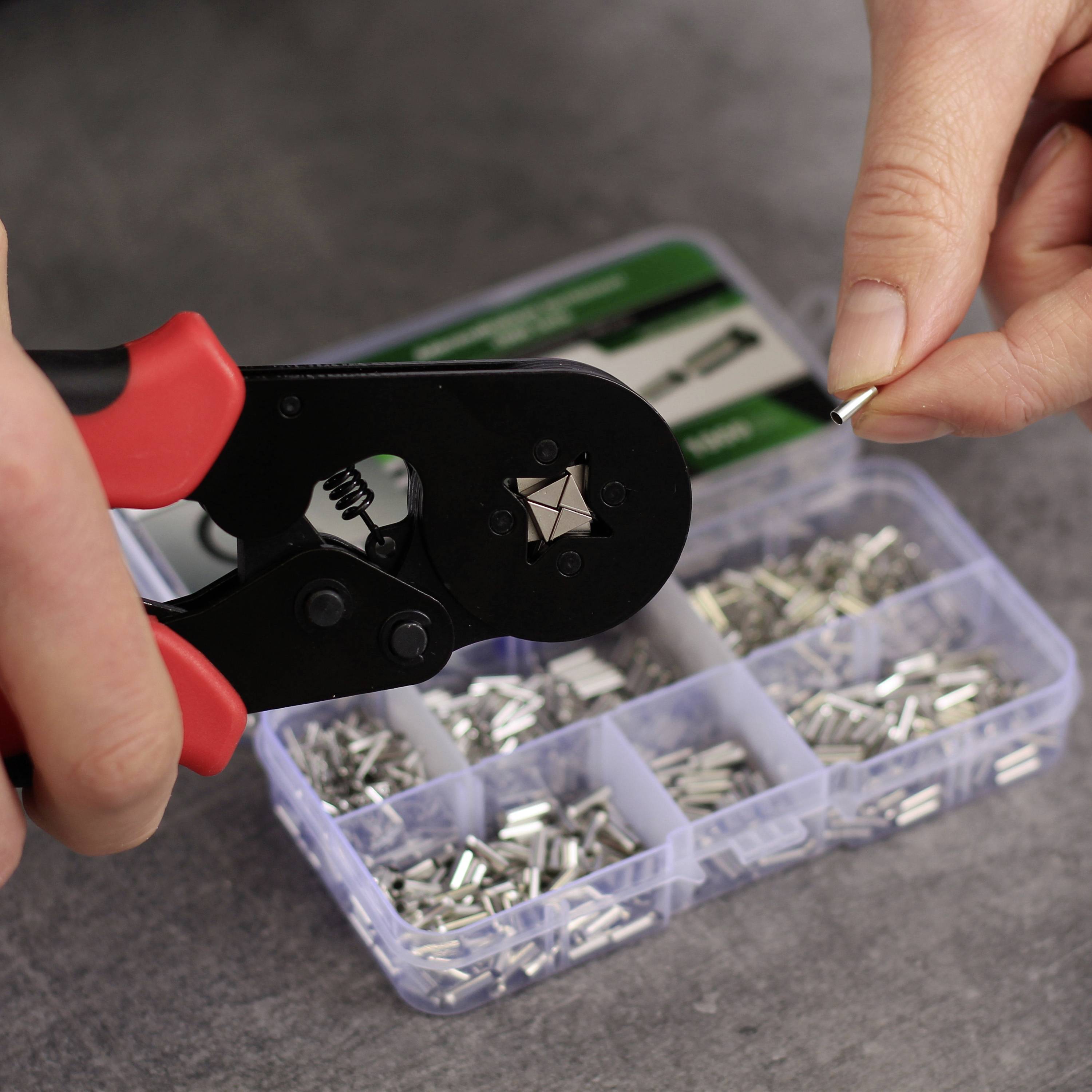 Una persona sta utilizzando una pinza crimpatrice per fissare un piccolo connettore metallico da un contenitore con diversi connettori.