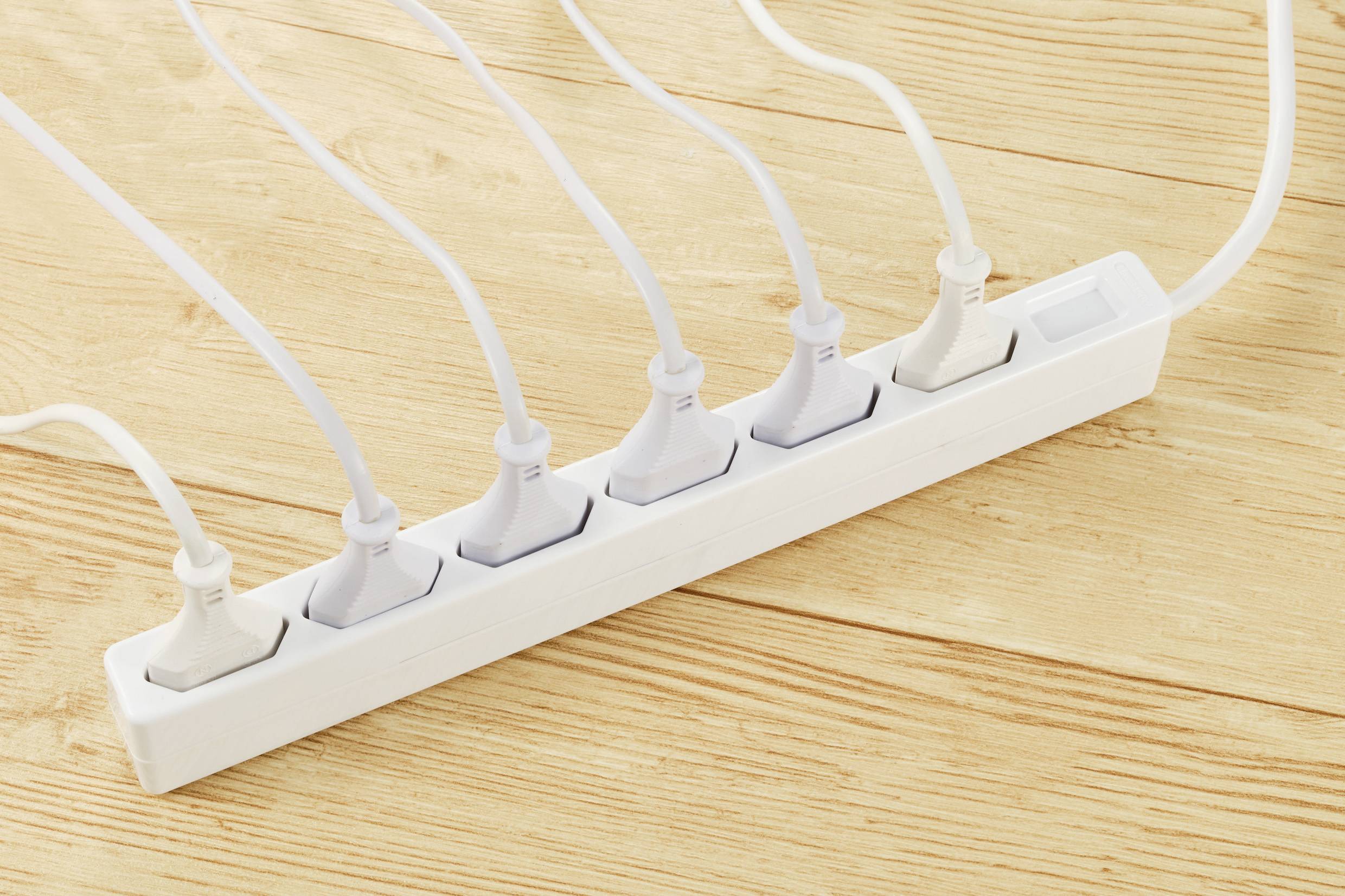 Multipresa con sei spine bianche inserite su un pavimento in legno.