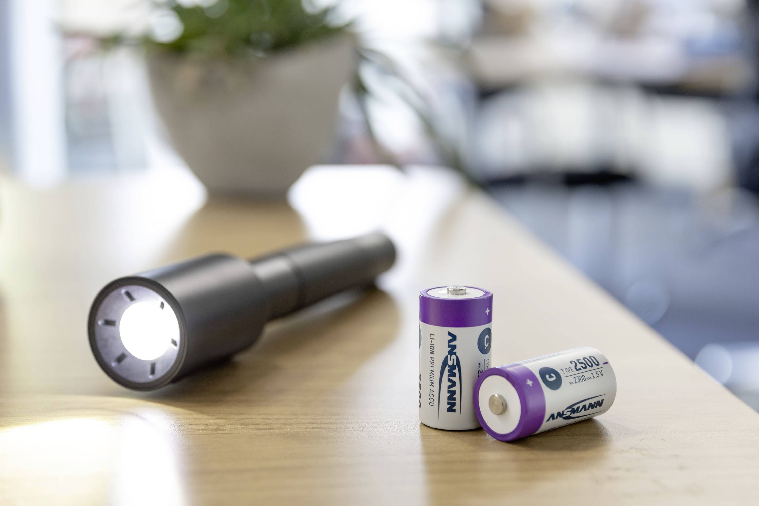 Una torcia illumina un tavolo. Accanto ci sono due batterie. Sullo sfondo si intravede una stanza chiara e sfocata.