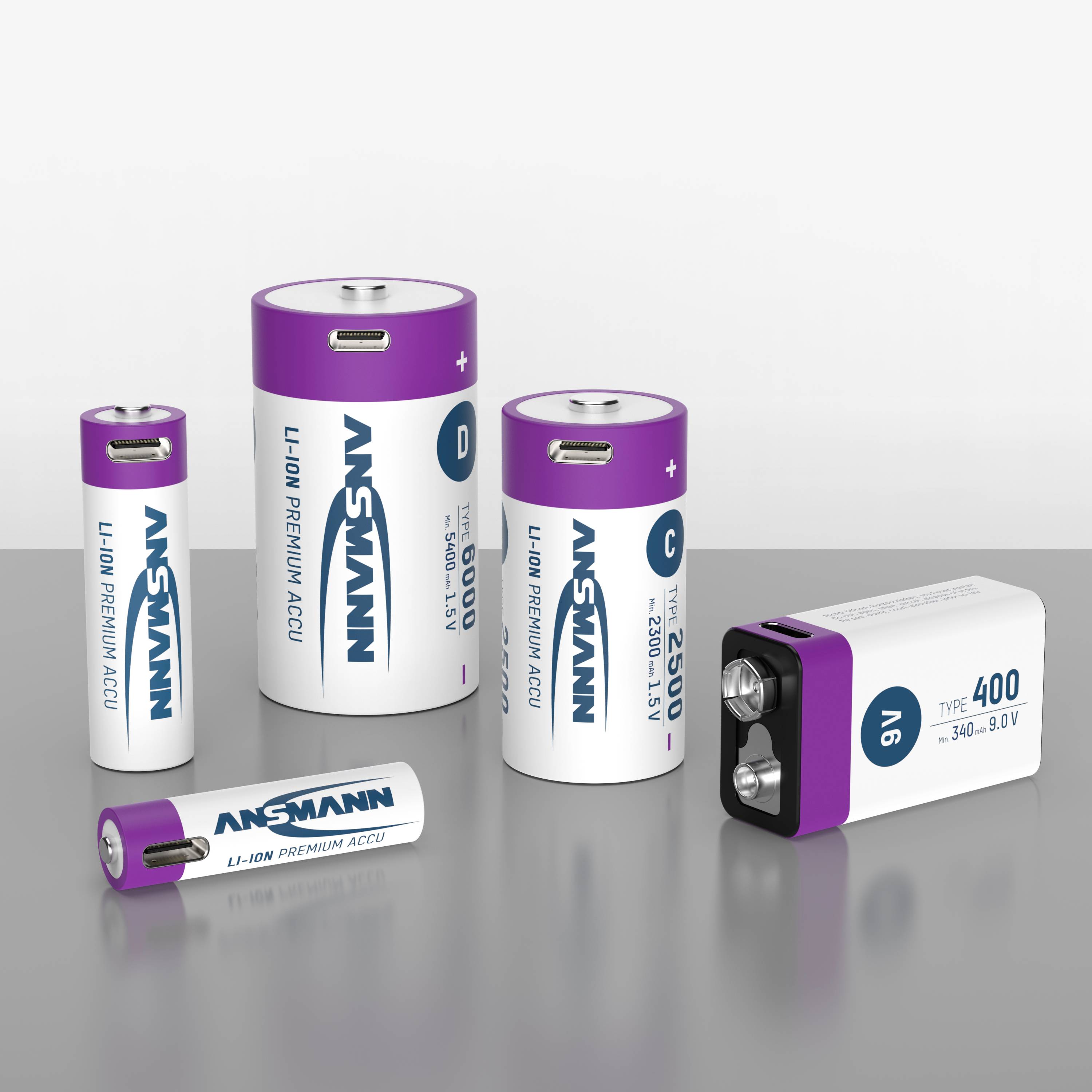 Cinque diversi tipi di batterie in un gruppo: AA, C, D, blocco da 9V e AAA. Tutte sono etichettate con 'ANSMANN' e hanno cappucci viola.