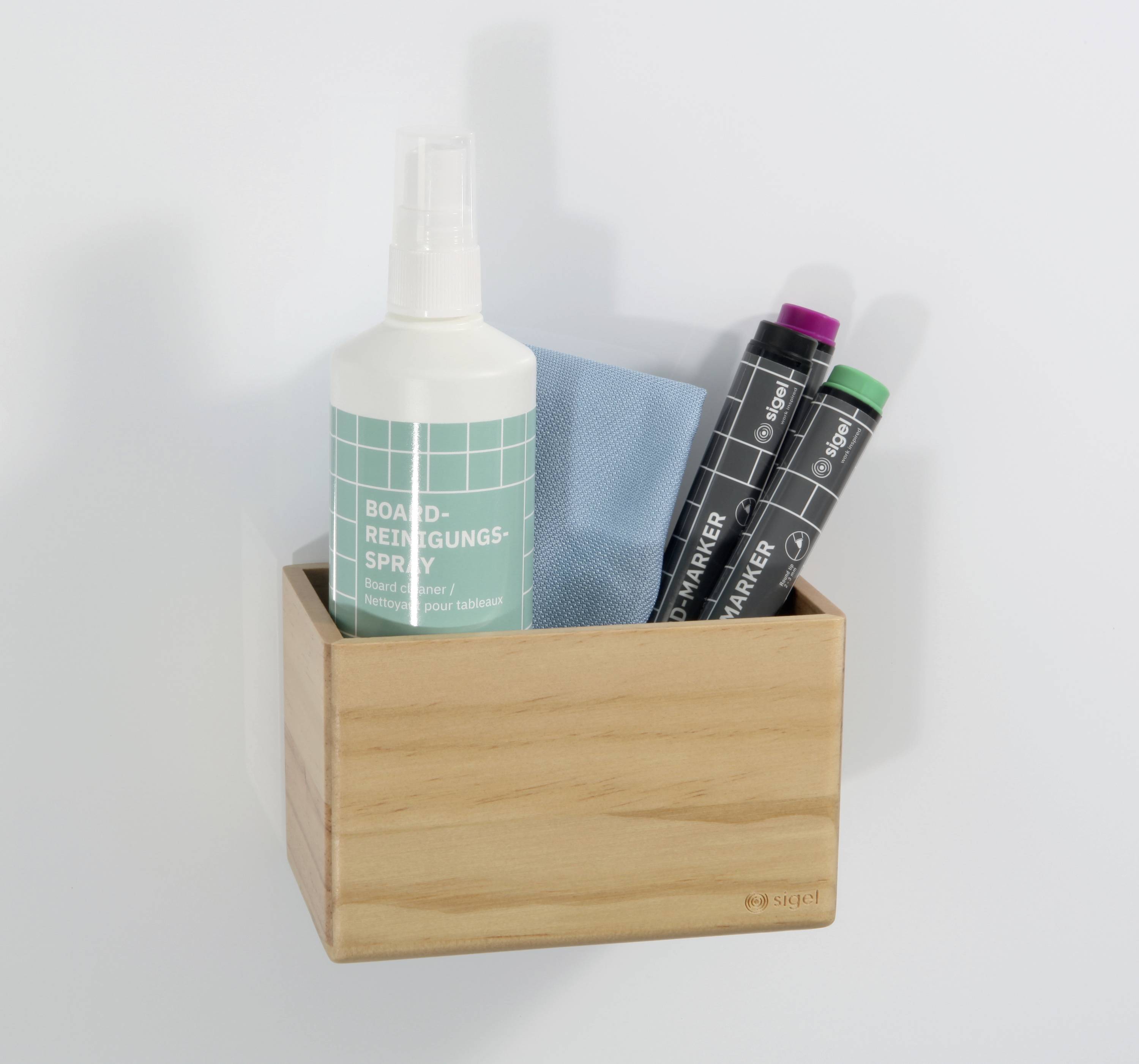 Una scatola di legno contiene un detergente spray, un panno blu e due pennarelli per lavagna. Sono appesi a una parete bianca.