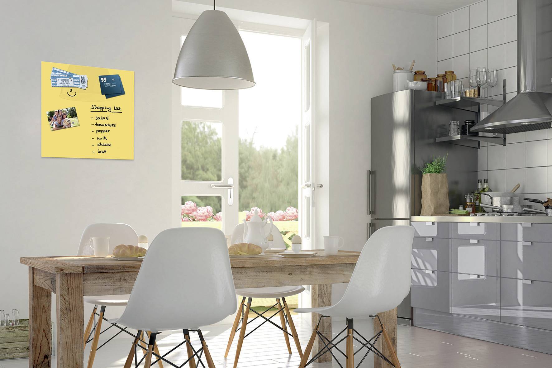 Una cucina moderna con un tavolo in legno e sedie bianche. Sulla parete è appesa una lavagna con una lista della spesa e una scheda ricetta.