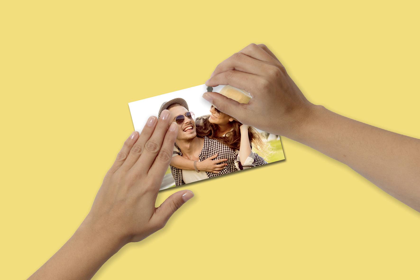 Una persona tiene in mano una foto di una coppia sorridente su uno sfondo giallo, che trasmette un'atmosfera felice e affettuosa.